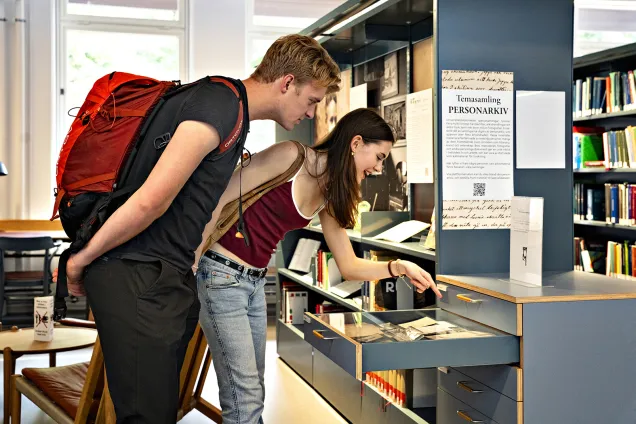 En man och en kvinna står och tittar på en temasamling på Universitetsbiblioteket.