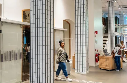 A student passes between two grey-and-white-checkered pillars on the entrance floor.