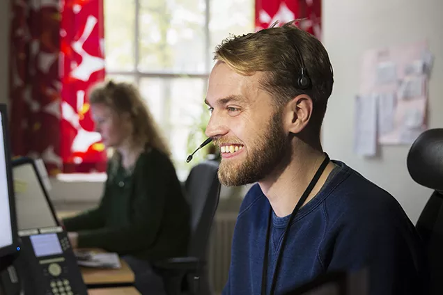 A smiling employee in a headset in front of a computer screen. Photographer Johan Bävman.