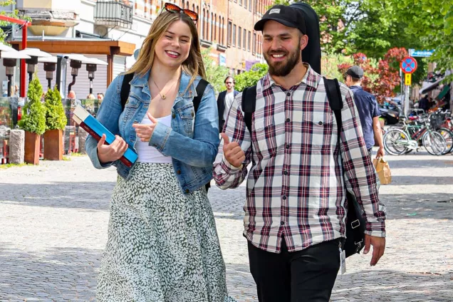 Two students walk next to each other and give thumbs up. Photographer Michel Thomas.