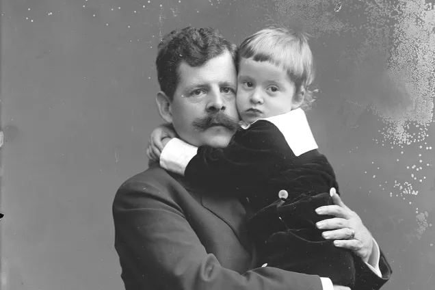 Man håller sin son i famnen. Pojken har armarna om pappans hals. Fotografi Per Bagge år 1917.