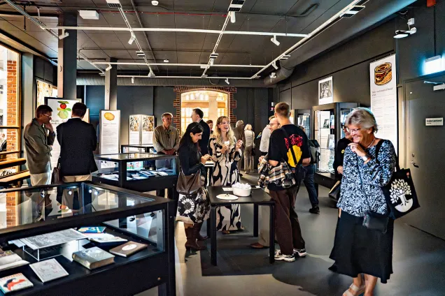 Glada människor fyller en sal med belysta glasmontrar och svartmålade väggar.