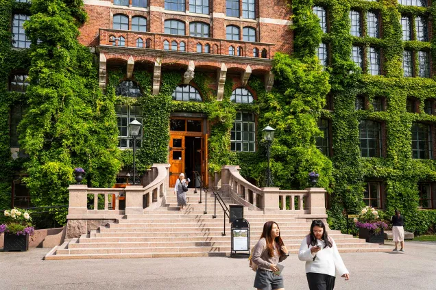 Stentrappa framför röd tegelbyggnad. Besökare går ner för trappan