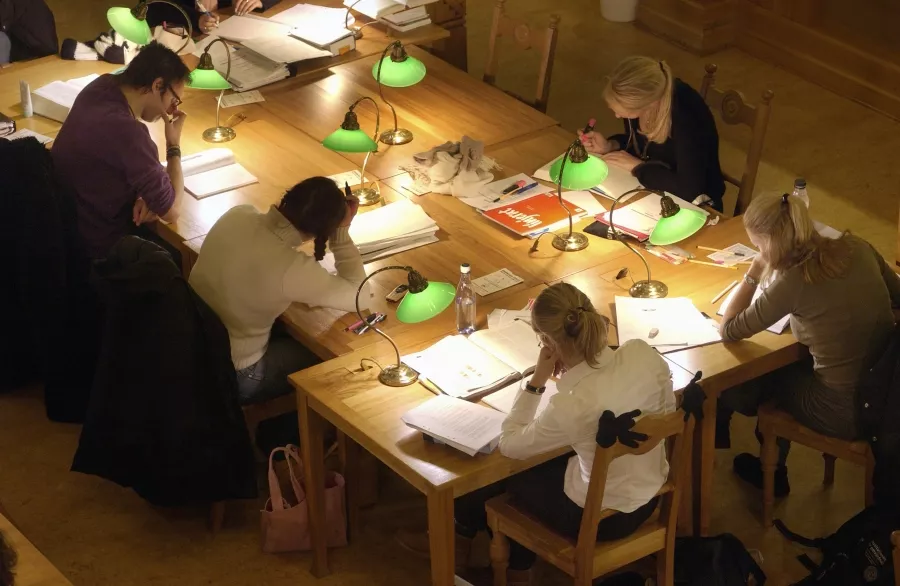 Studenter studerar runt ett stort bord med gröna bordslampor.